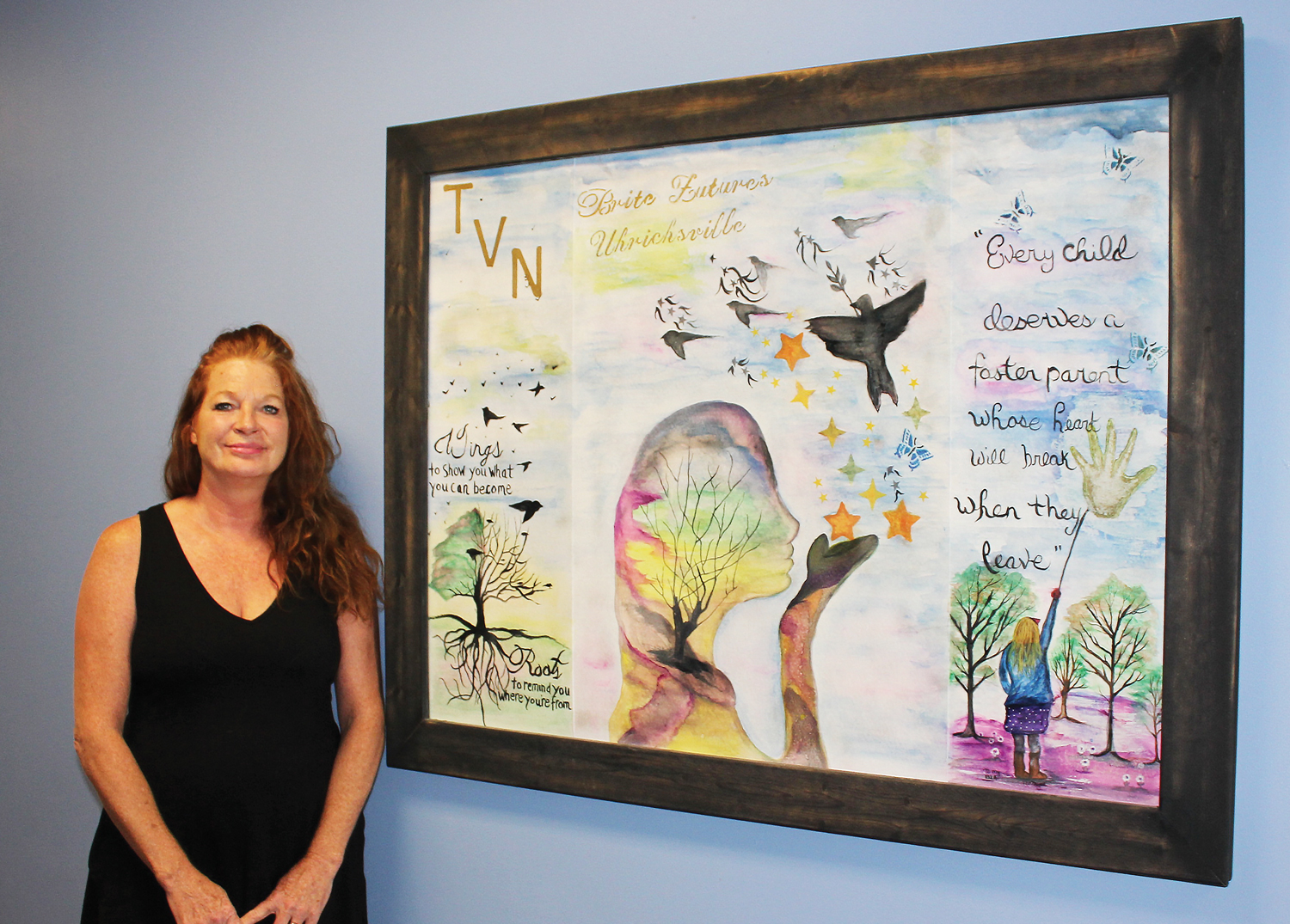 Melinda Stutler, TVN foster parent and artist, stands with a custom piece on the hallway wall of the Uhrichsville office.