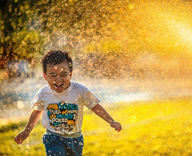 happy boy running through sprinkler